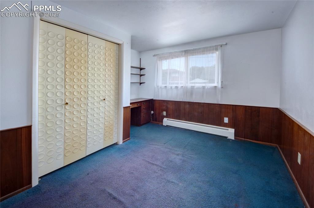 Image 24 of 37: Unfurnished bedroom with wood walls, wainscoting, baseboard heating, and ca