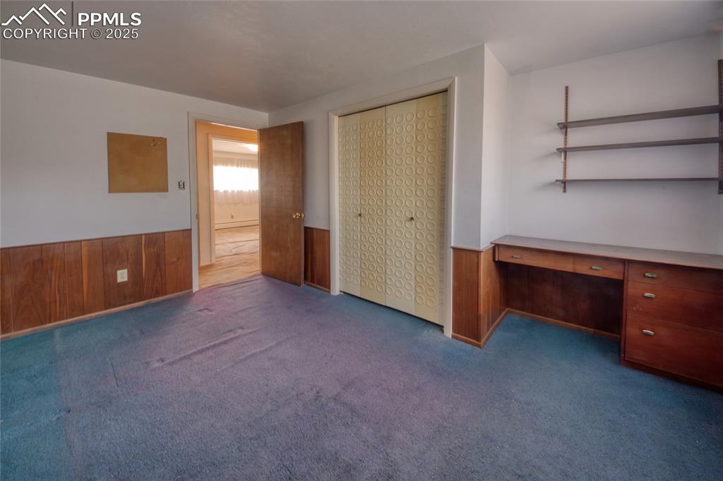Image 25 of 37: Unfurnished bedroom featuring wooden walls, an office area, carpet floors,