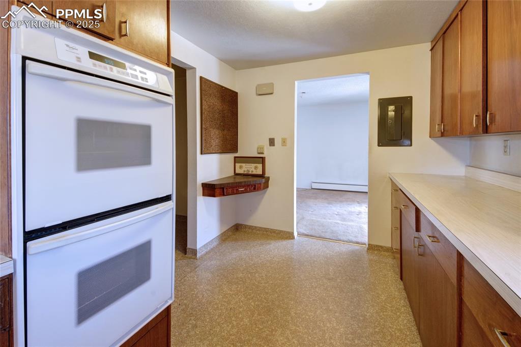 Image 9 of 37: Kitchen featuring double oven, electric panel, brown cabinetry, and a baseb