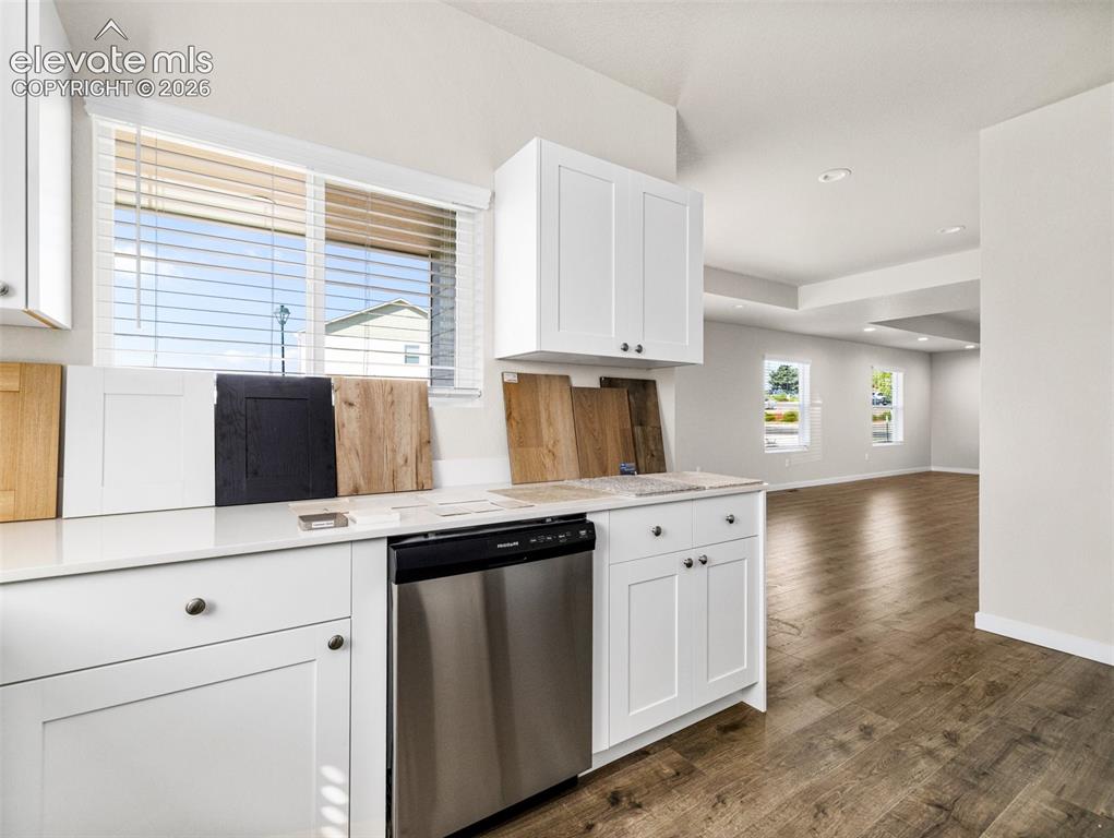 Image 22 of 30: White cabinetry with dark hardware, stainless steel dishwasher, and light c