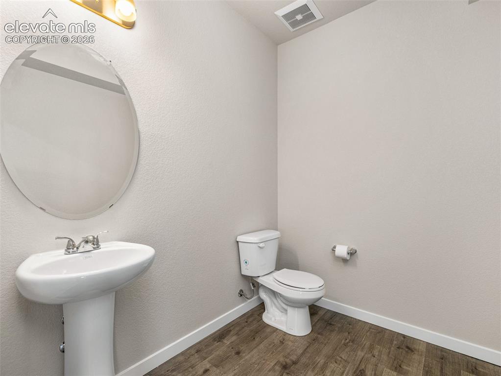 Image 23 of 30: Pedestal sink with chrome faucet, oval mirror, toilet, and wood-finish floo