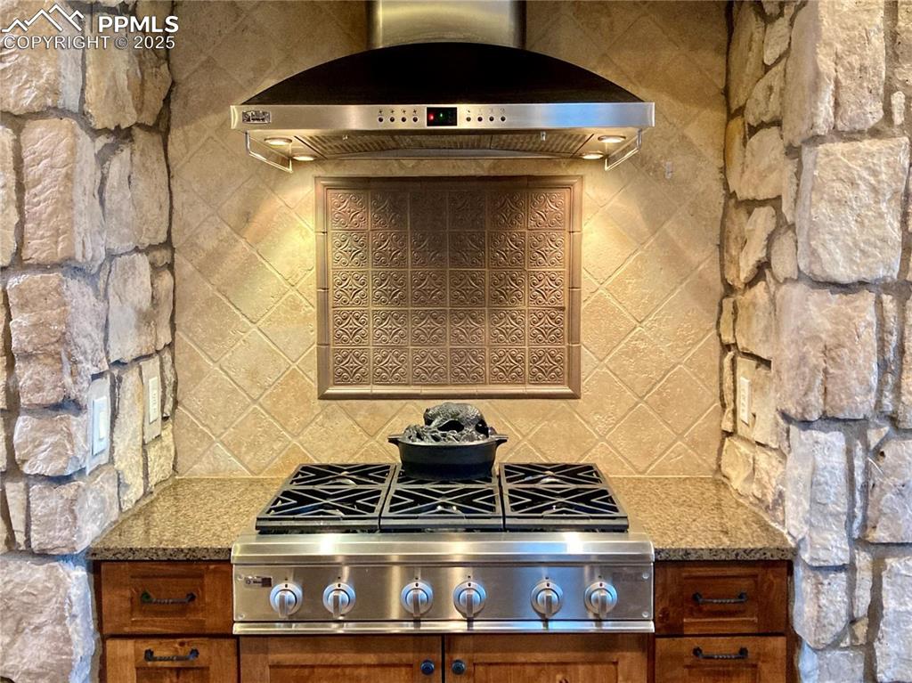Image 11 of 50: The 6-burner gas stove with steel hood and custom backsplash is enclosed wi
