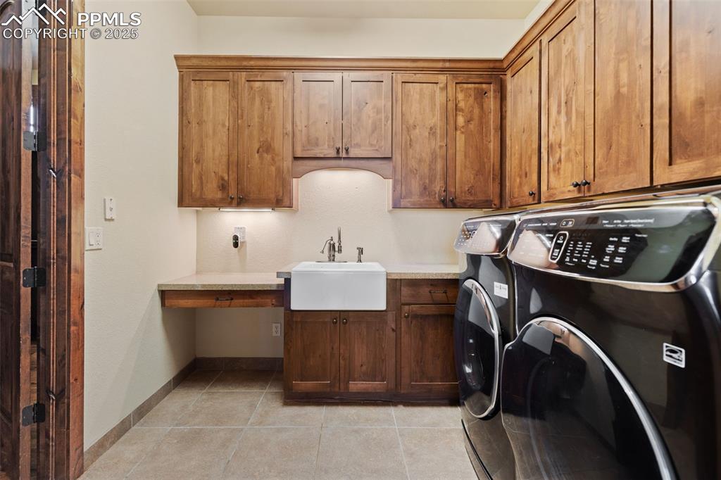 Image 27 of 50: The tiled main level laundry includes a farmhouse sink, cabinetry, granite
