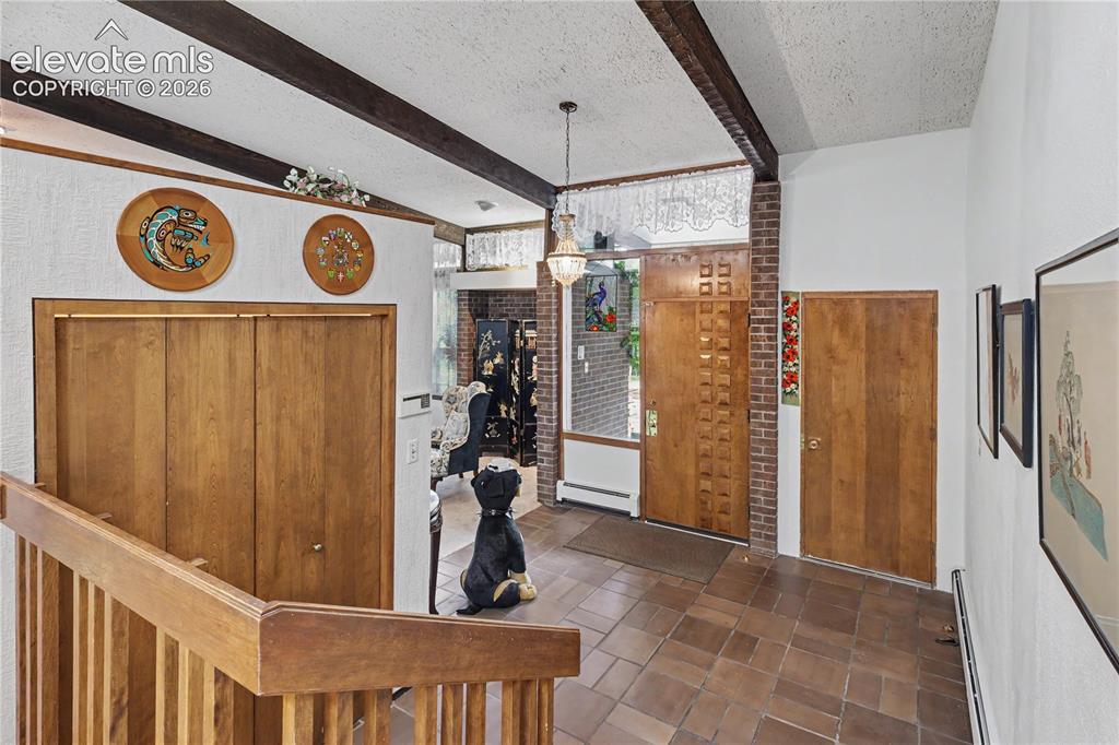 Image 12 of 50: Foyer featuring exposed ceiling beams, wood-finish doors, brick accents, ce