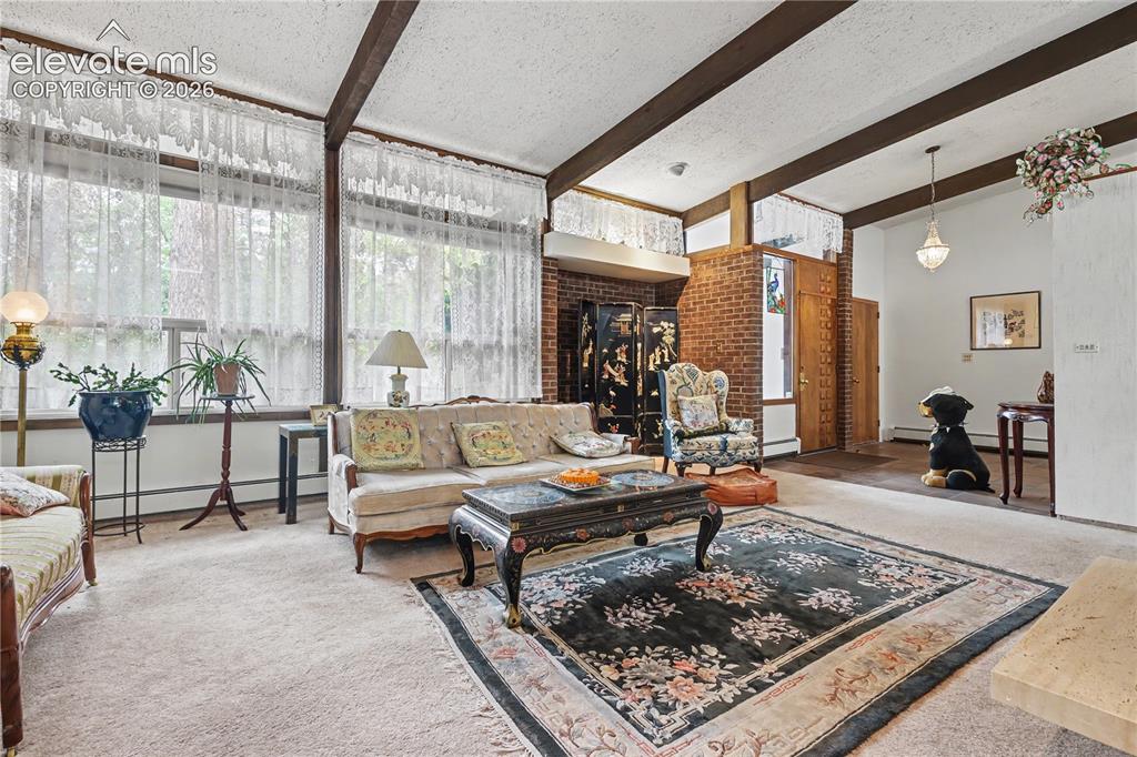 Image 18 of 50: Spacious living area featuring exposed ceiling beams, extensive window fron