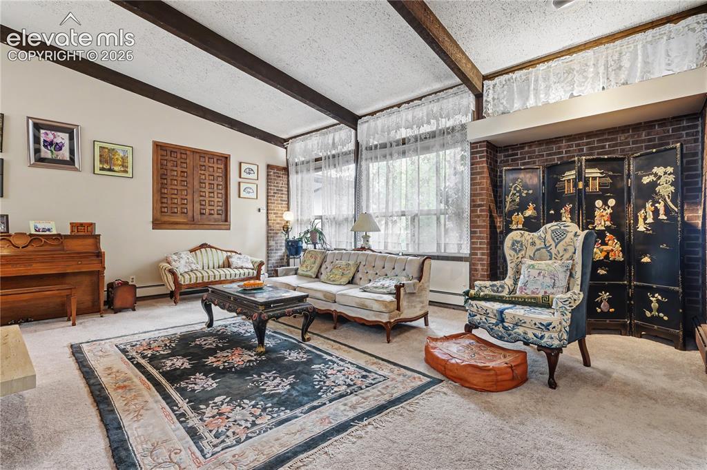 Image 19 of 50: Living area featuring exposed ceiling beams, brick accent walls, and large 