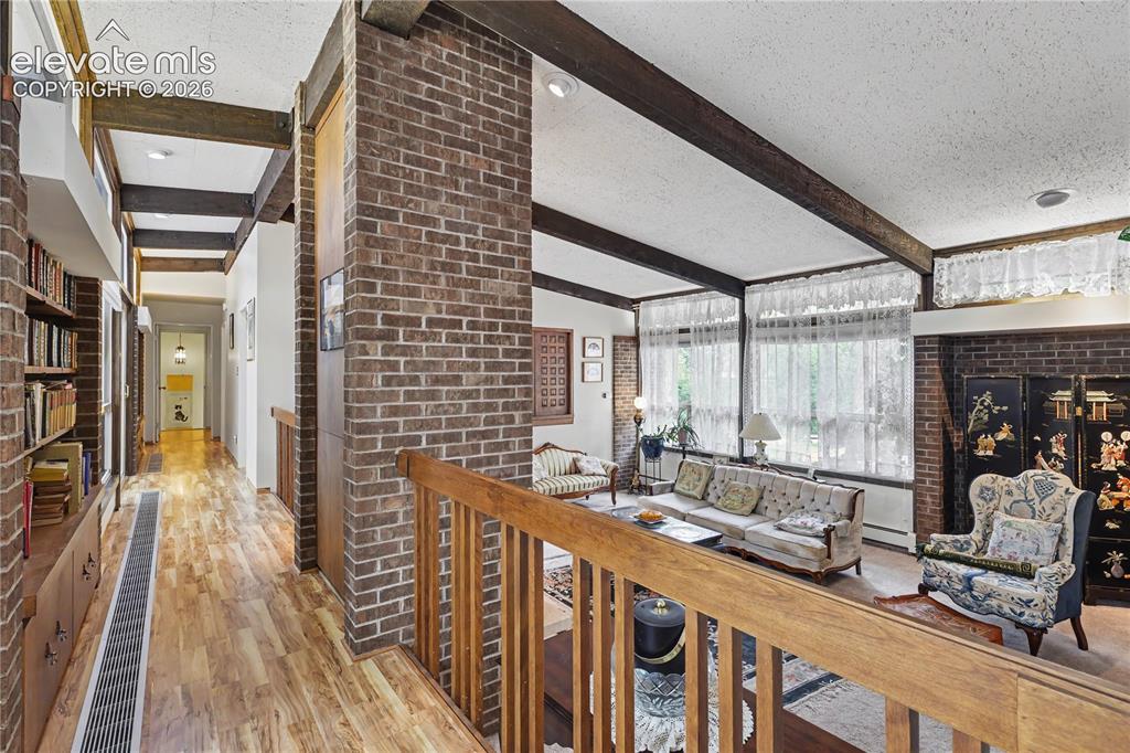 Image 23 of 50: Brick column accents a living space with exposed ceiling beams and large wi