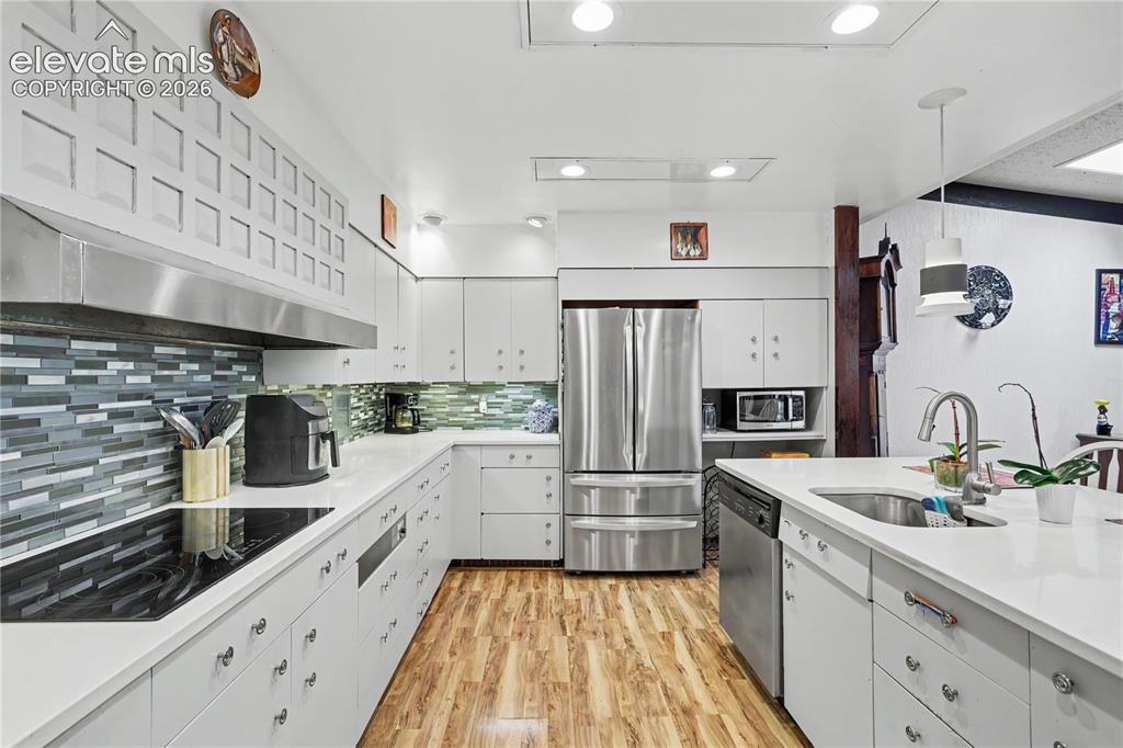 Image 27 of 50: Kitchen featuring white cabinetry, wood-finish flooring, stainless steel ap