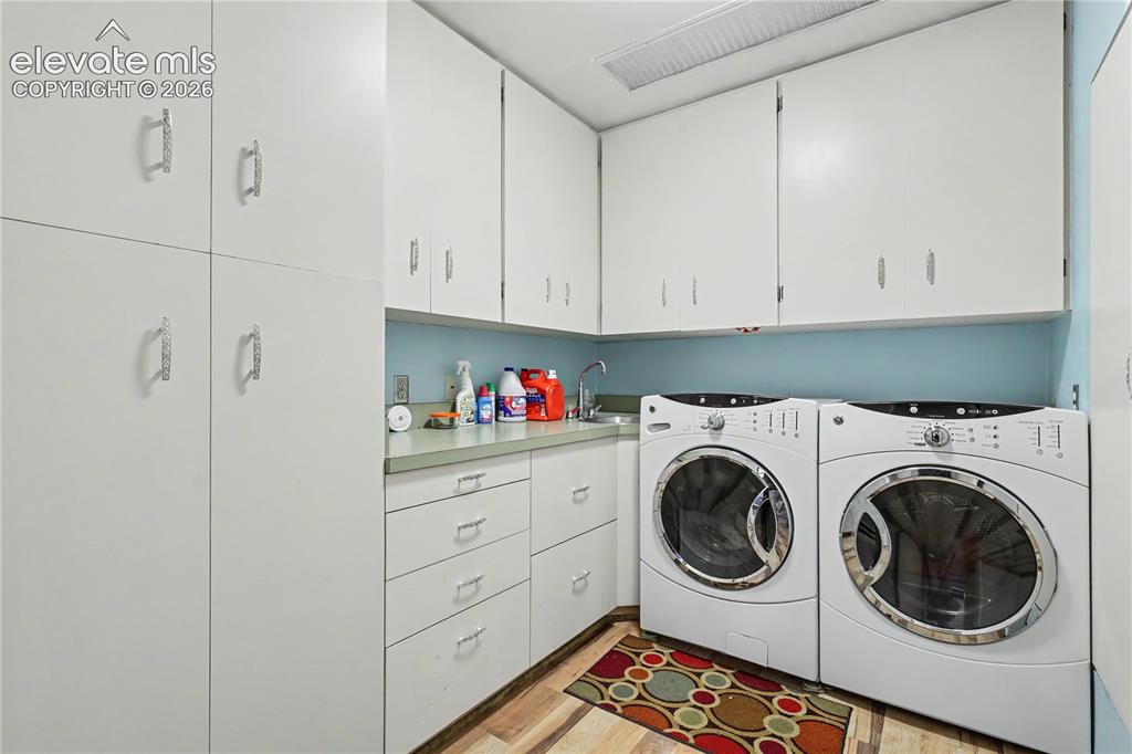 Image 30 of 50: Laundry room featuring white cabinetry, a built-in sink, and laminate wood-