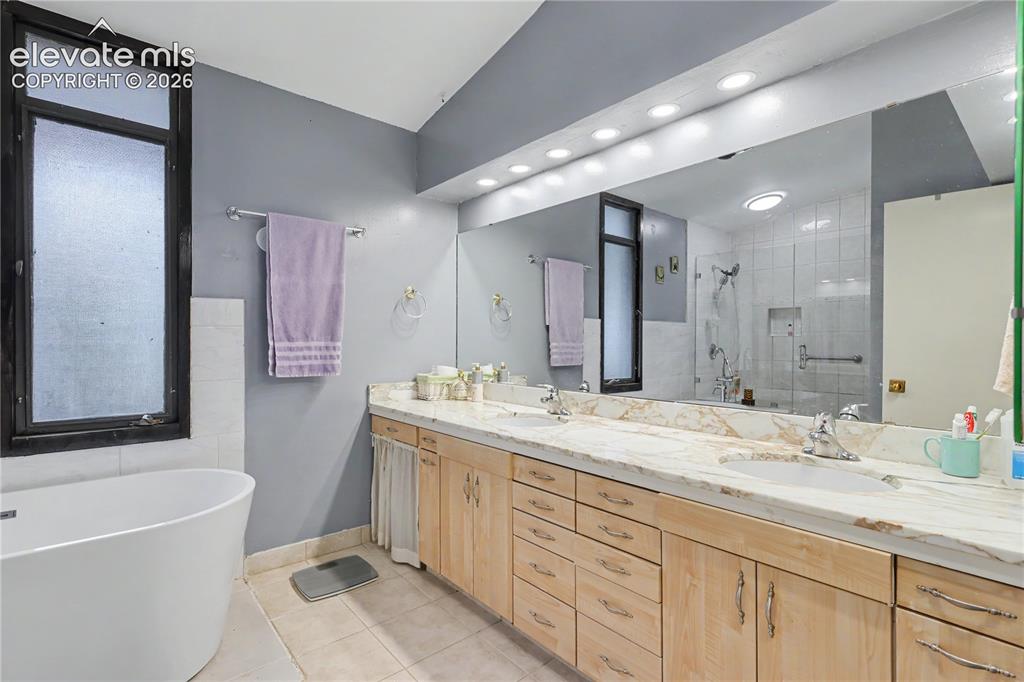 Image 34 of 50: Dual vanity with light wood cabinetry, stone countertops, and integrated si
