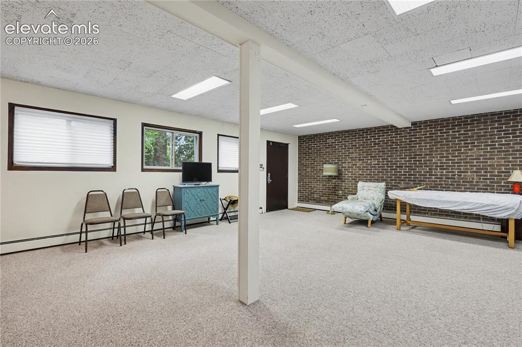 Image 45 of 50: Spacious room featuring light-toned carpeting, a partial brick accent wall,