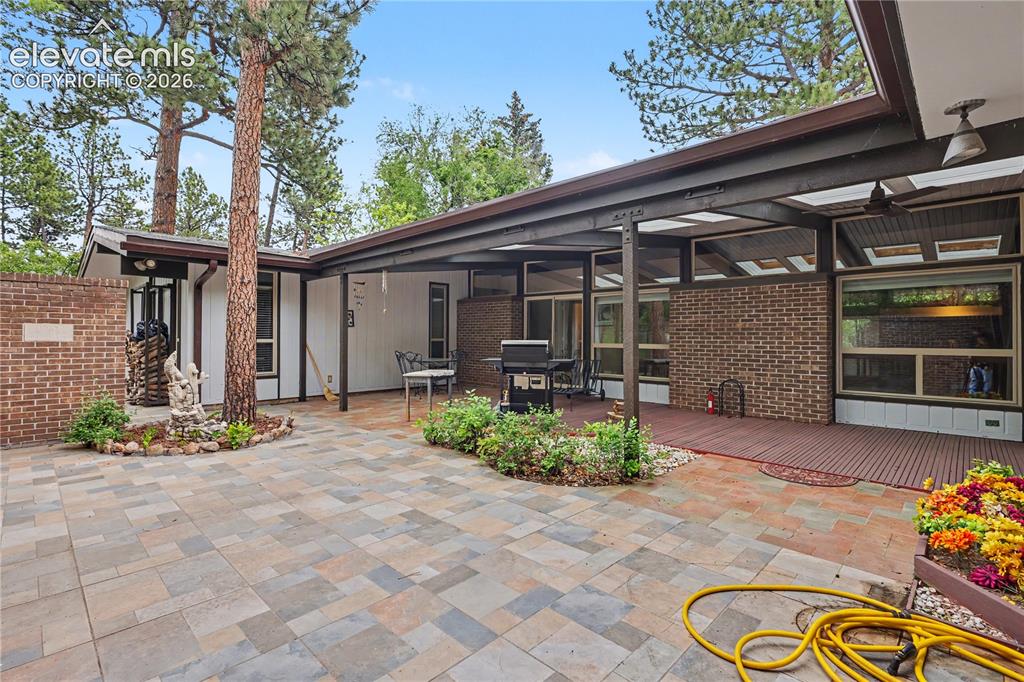 Image 50 of 50: Expansive multi-tone paver patio area with a covered deck featuring a wood-