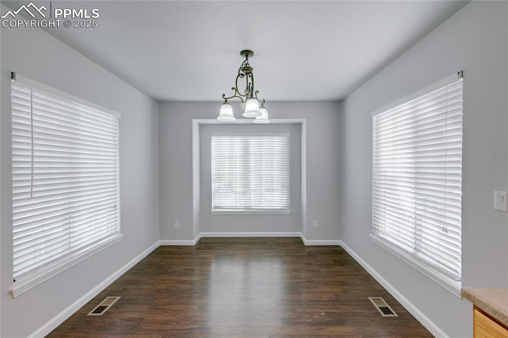 Image 9 of 23: Empty room featuring a chandelier and dark wood-style flooring