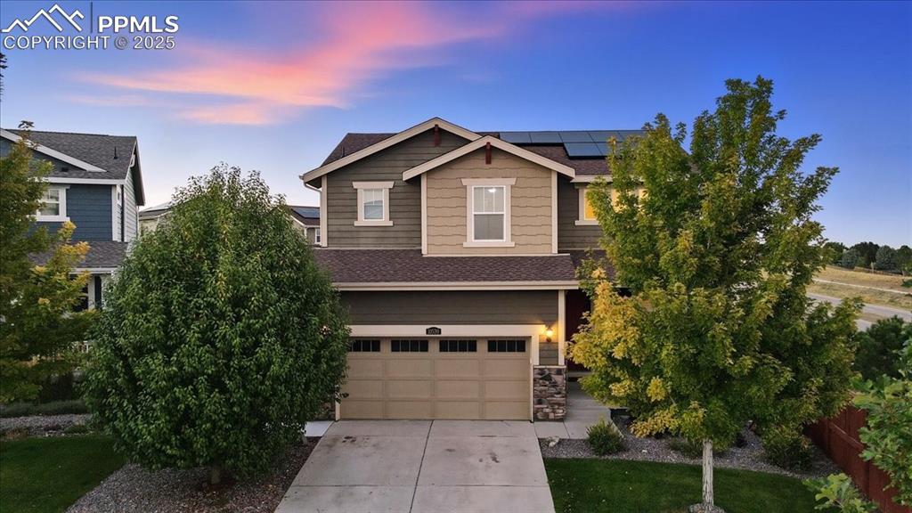 Caption: View of front of home with a shingled roof, concrete driveway, roof mounted solar panels, stone sidi