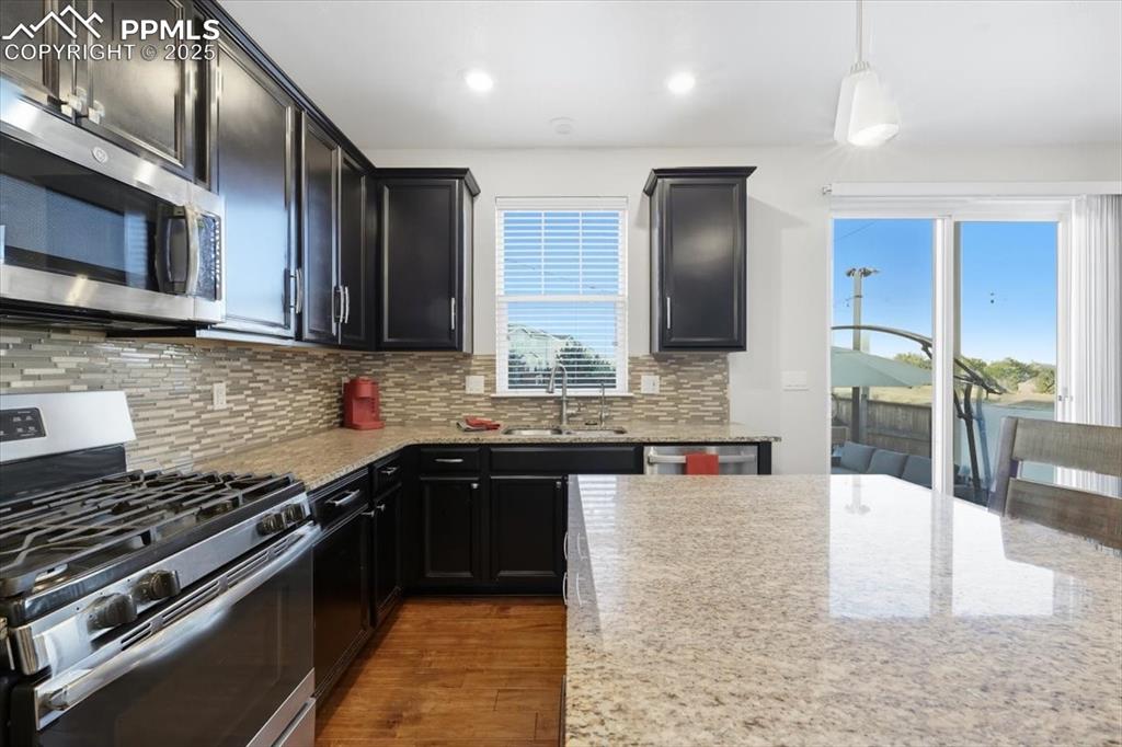 Image 6 of 35: Kitchen with stainless steel appliances, backsplash, light stone counters,