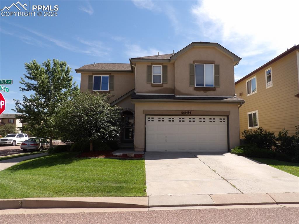 Caption: Traditional home featuring stucco siding, a front yard, driveway, and an attached garage