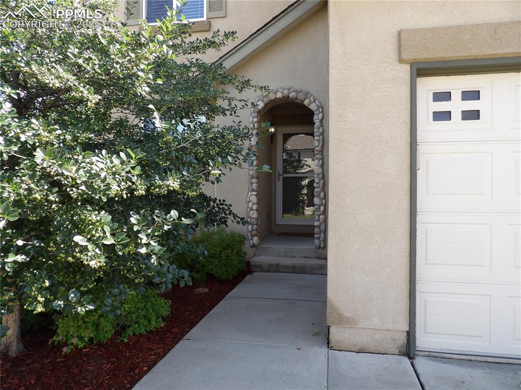 Image 2 of 23: Doorway to property featuring stucco siding and a garage