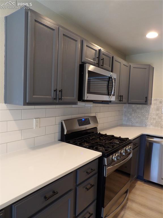 Image 7 of 23: Kitchen with range, dishwashing machine, light wood-style floors, light cou