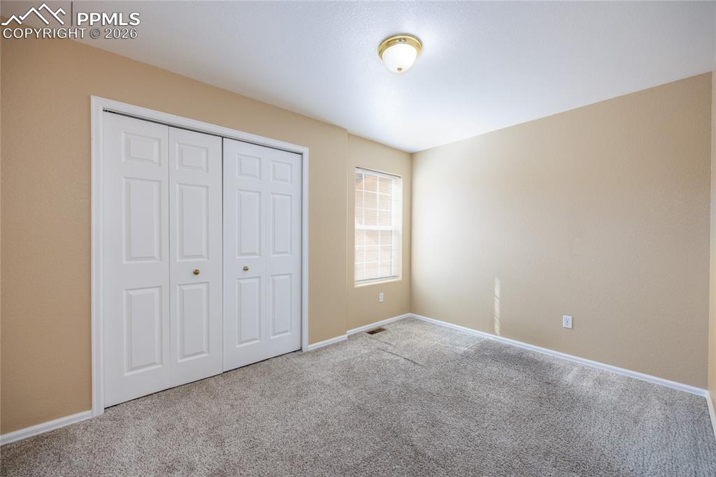 Image 19 of 25: Carpeted room featuring a window with blinds, white bi-fold closet doors, a