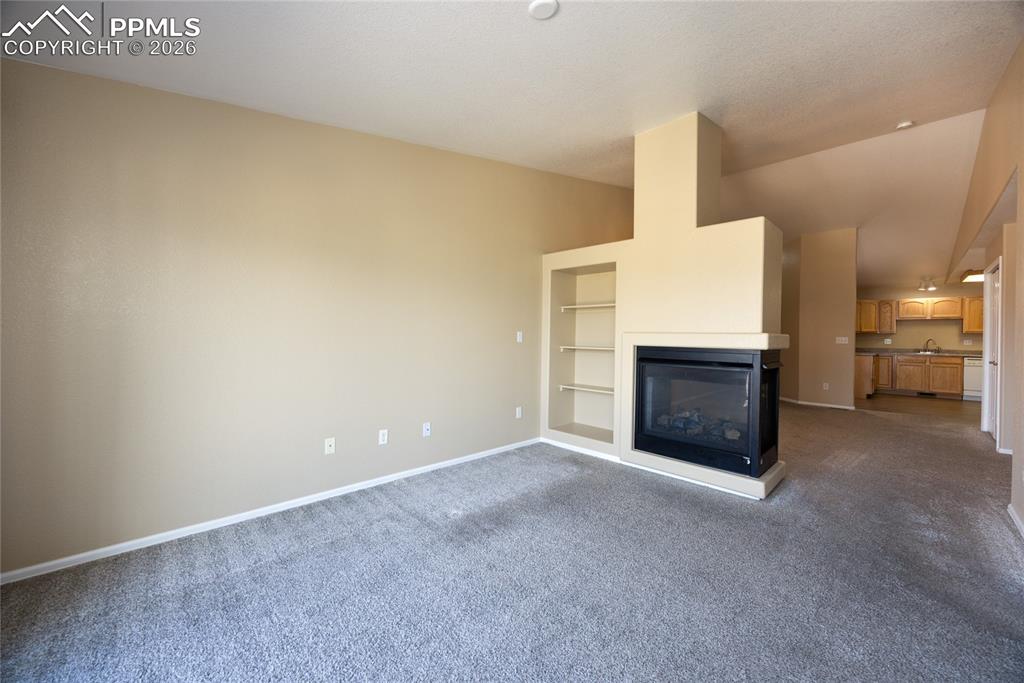 Image 9 of 25: Living area featuring a built-in fireplace, integrated shelving, neutral wa