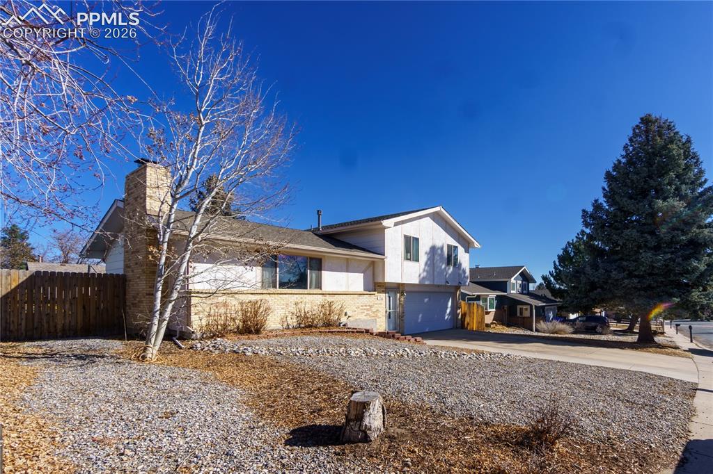 Image 1 of 25: Split level home with an attached garage, a chimney, fence, brick siding, a