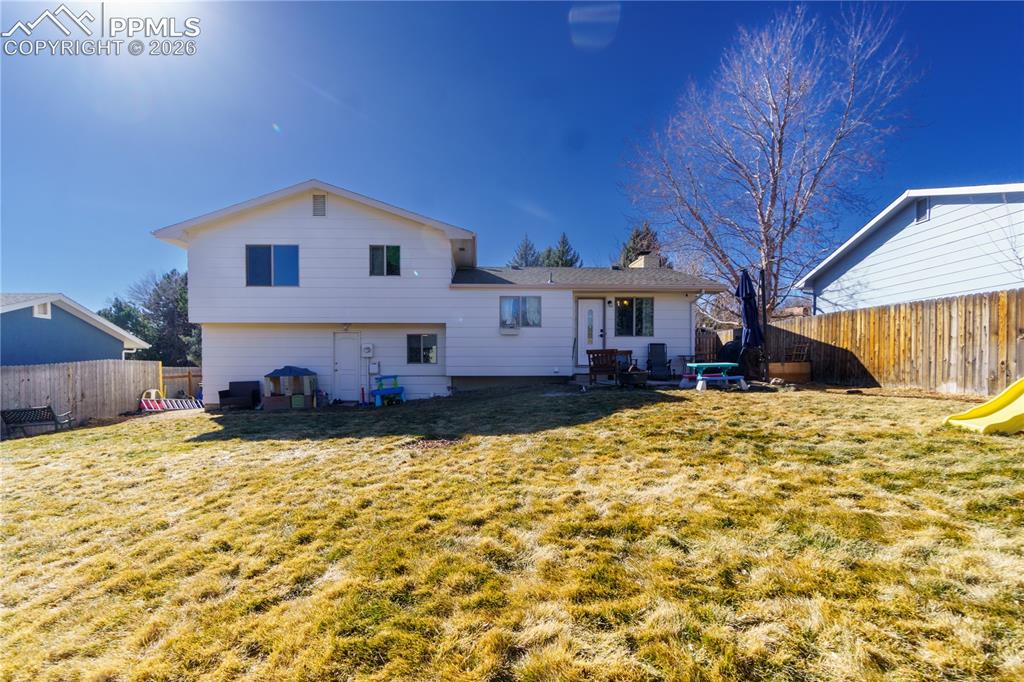 Image 24 of 25: Back of property with entry steps, a fenced backyard, a chimney, and a lawn