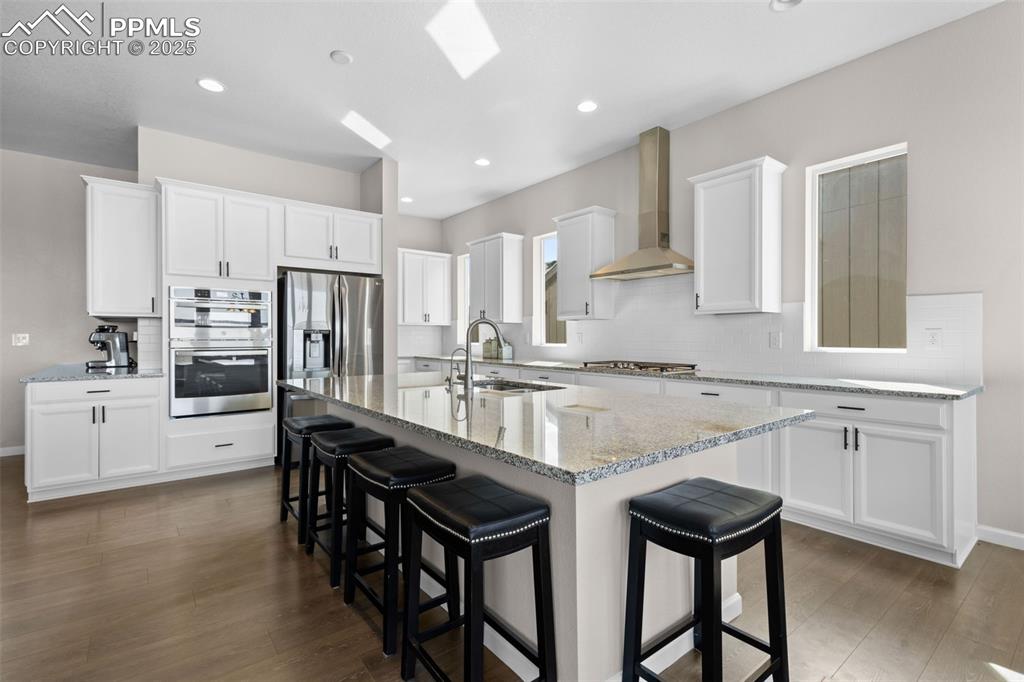 Image 10 of 47: Kitchen featuring a breakfast bar, white cabinetry, an island with sink, do