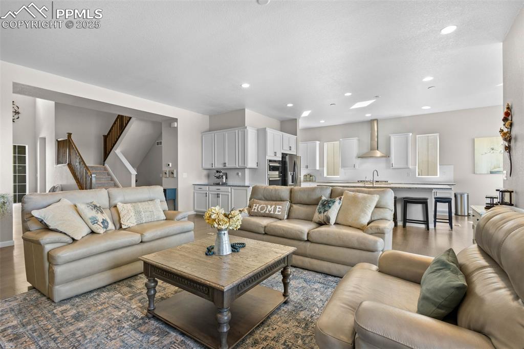 Image 12 of 47: Living room with wood finished floors, stairs, and recessed lighting