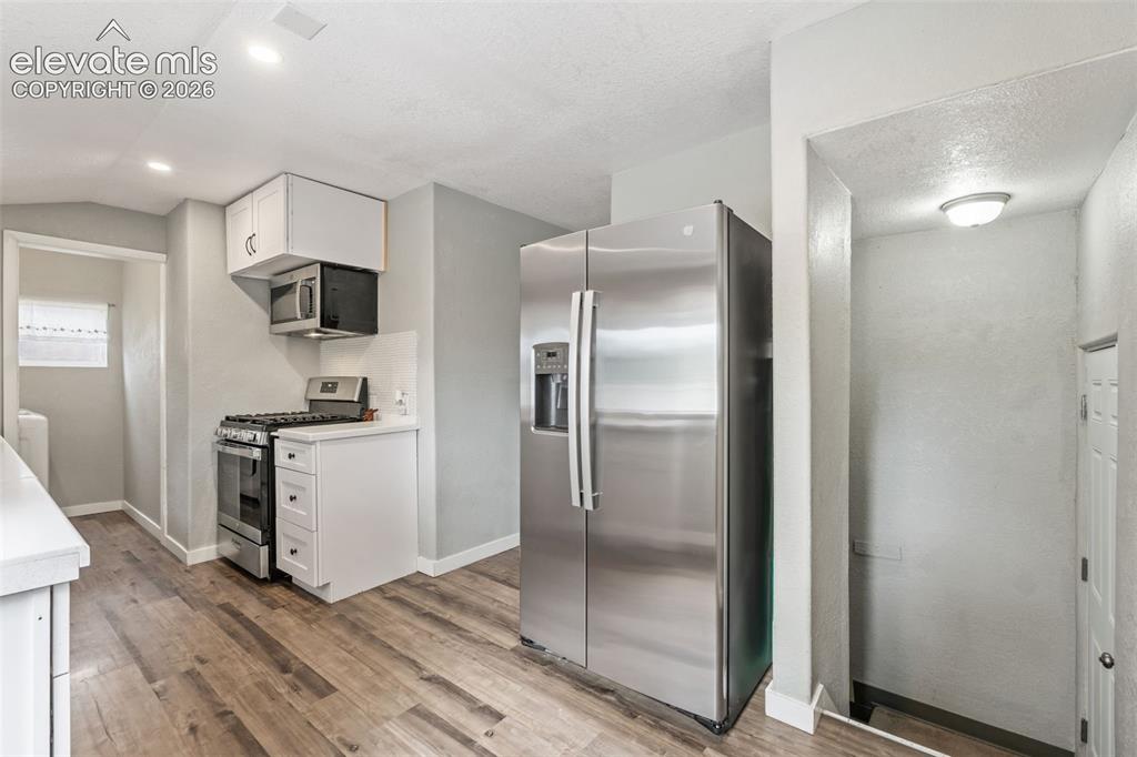 Image 17 of 50: Kitchen featuring wood-finish flooring, white cabinetry, and stainless stee