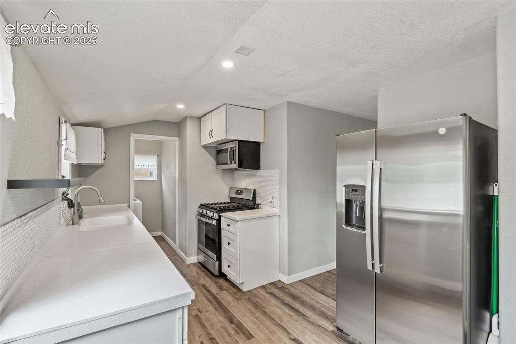 Image 18 of 50: Kitchen featuring white cabinetry, light countertops, wood-finish flooring,