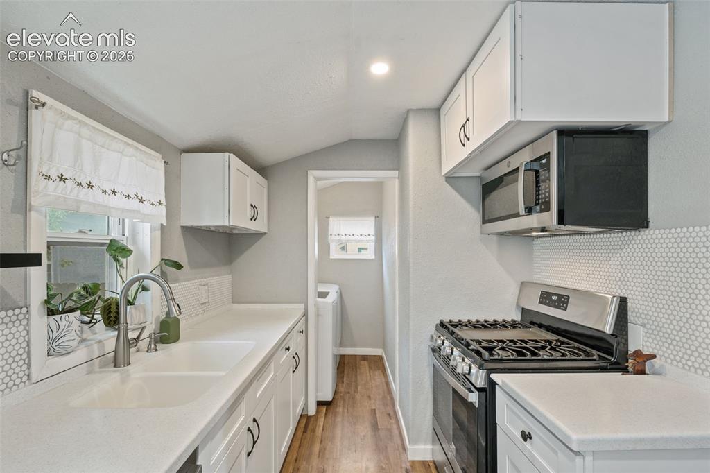 Image 5 of 50: Kitchen featuring wood-finish flooring, white cabinetry with dark hardware,
