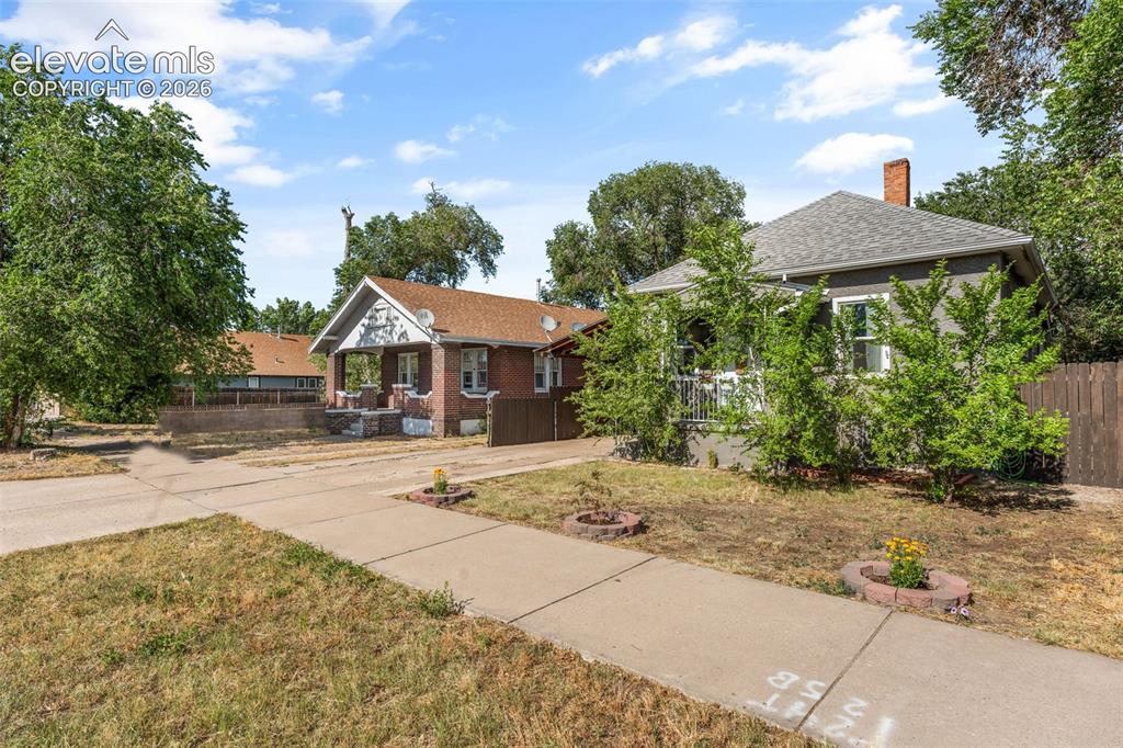 Image 7 of 50: Traditional bungalow with grey siding, a front porch, and a brick chimney