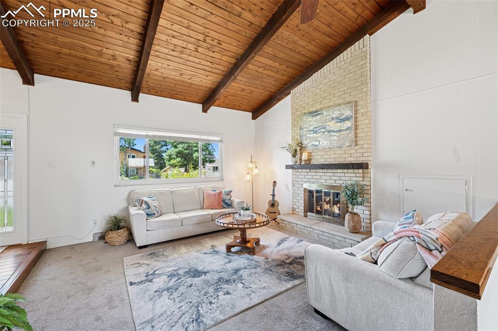 Image 19 of 34: Living room with a wooden ceiling with exposed beams, carpet floors, a fire
