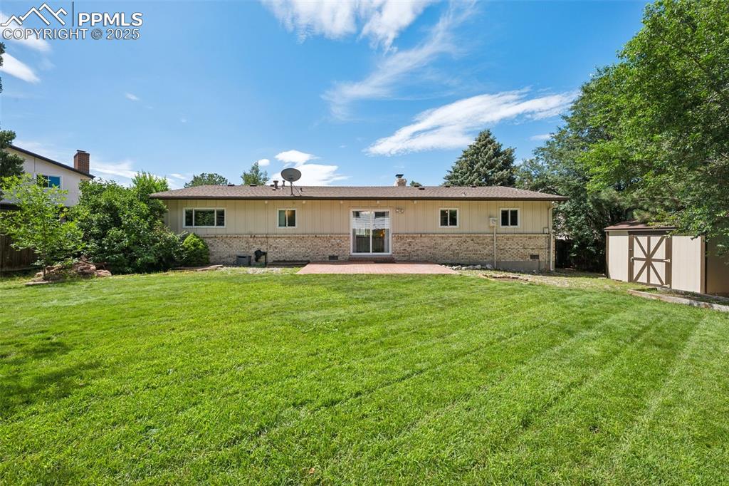 Image 5 of 34: Rear view of house with brick siding, a storage unit, a patio area, and a l