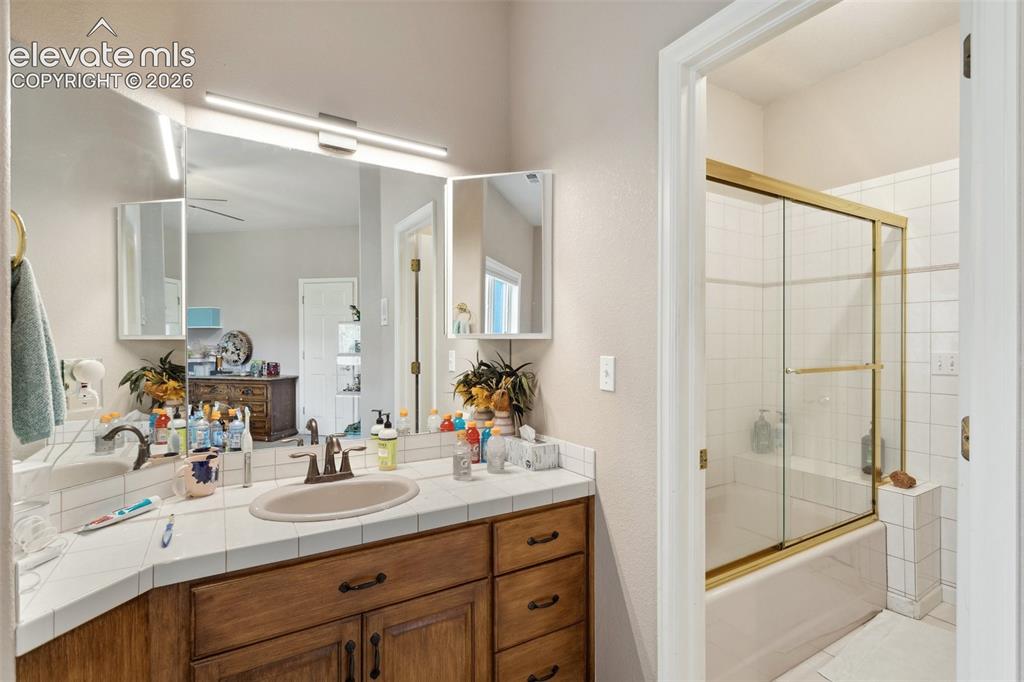 Image 40 of 50: Bathroom vanity featuring a single basin, tile countertop, and wood-finish
