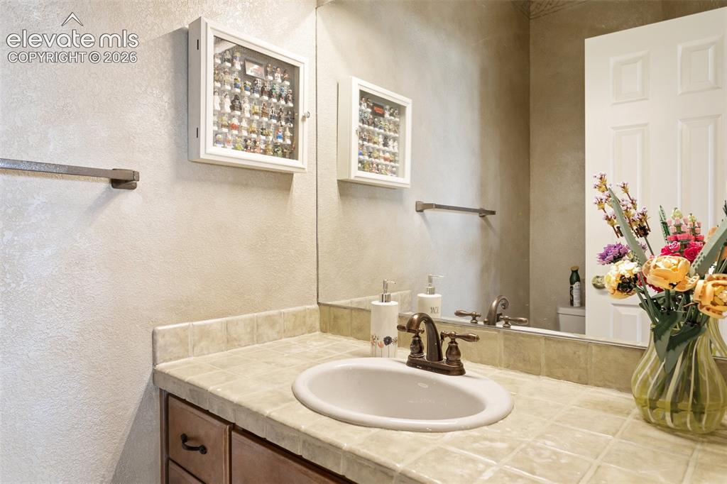 Image 44 of 50: Bathroom vanity featuring a tiled countertop, integrated sink, and bronze-f