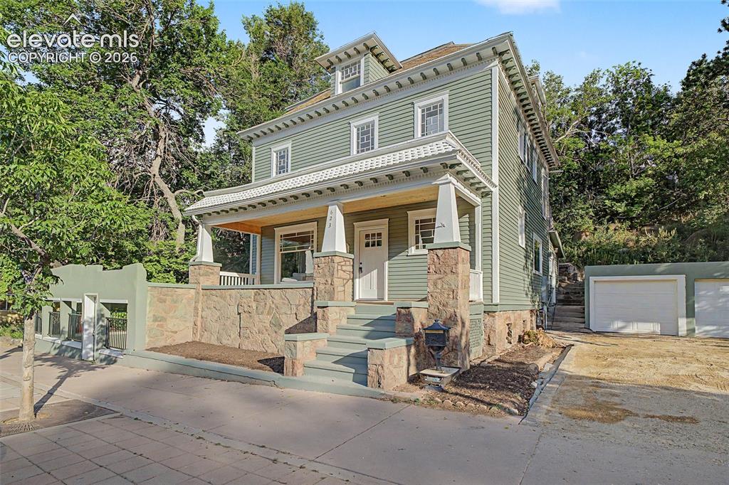Image 1 of 38: Three-story residence featuring sage green siding and natural stone accents