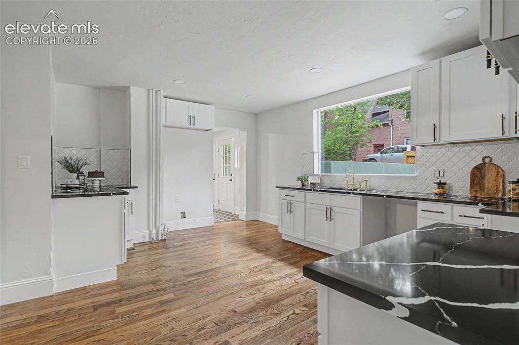Image 10 of 38: Spacious kitchen featuring expansive wood-finish flooring, white cabinetry,