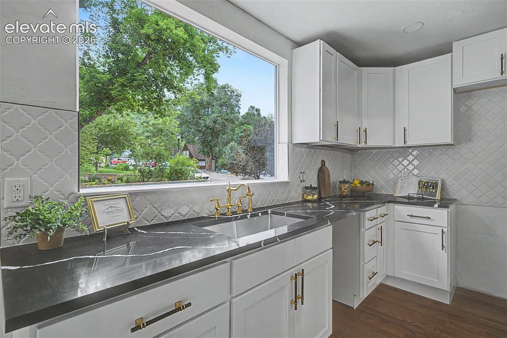 Image 11 of 38: Kitchen featuring white shaker-style cabinetry, dark countertops with light