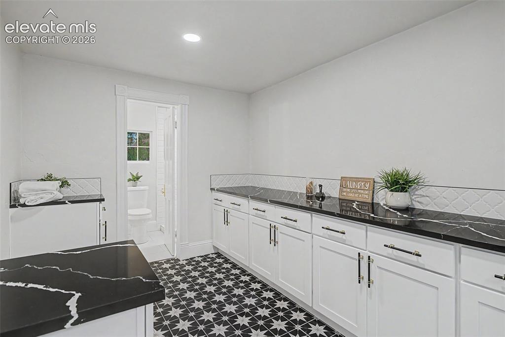 Image 15 of 38: Spacious utility room featuring patterned tile flooring, extensive black co