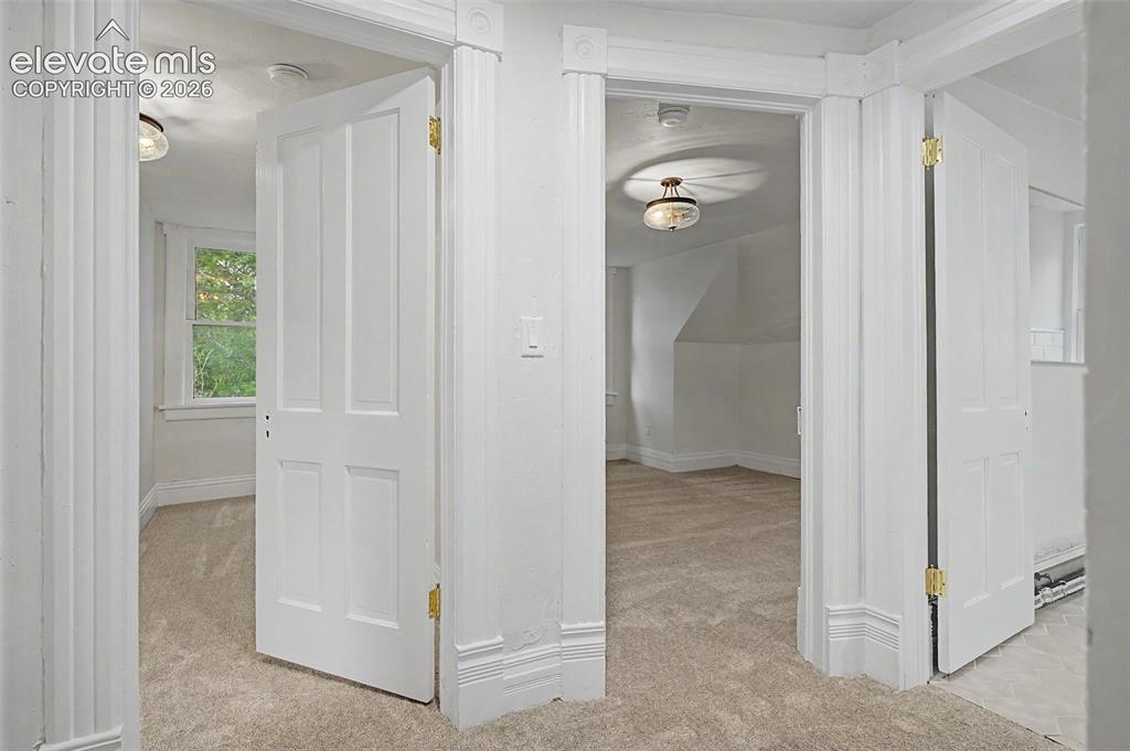 Image 28 of 38: An interior hallway featuring three white paneled doors, light beige carpet