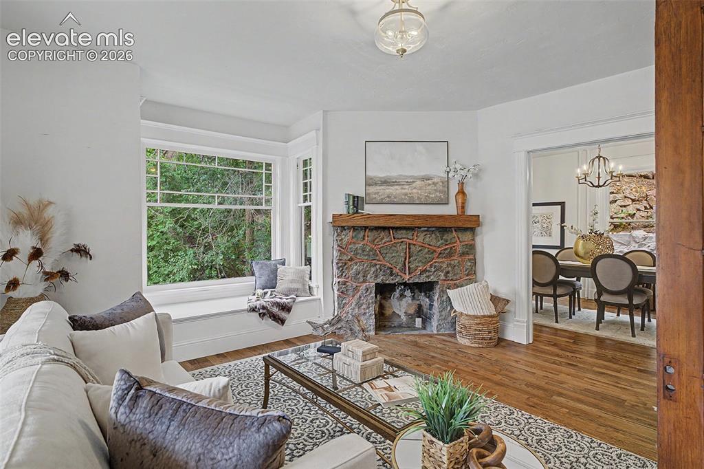 Image 6 of 38: Living area featuring a stone fireplace with a wood mantle, a spacious bay
