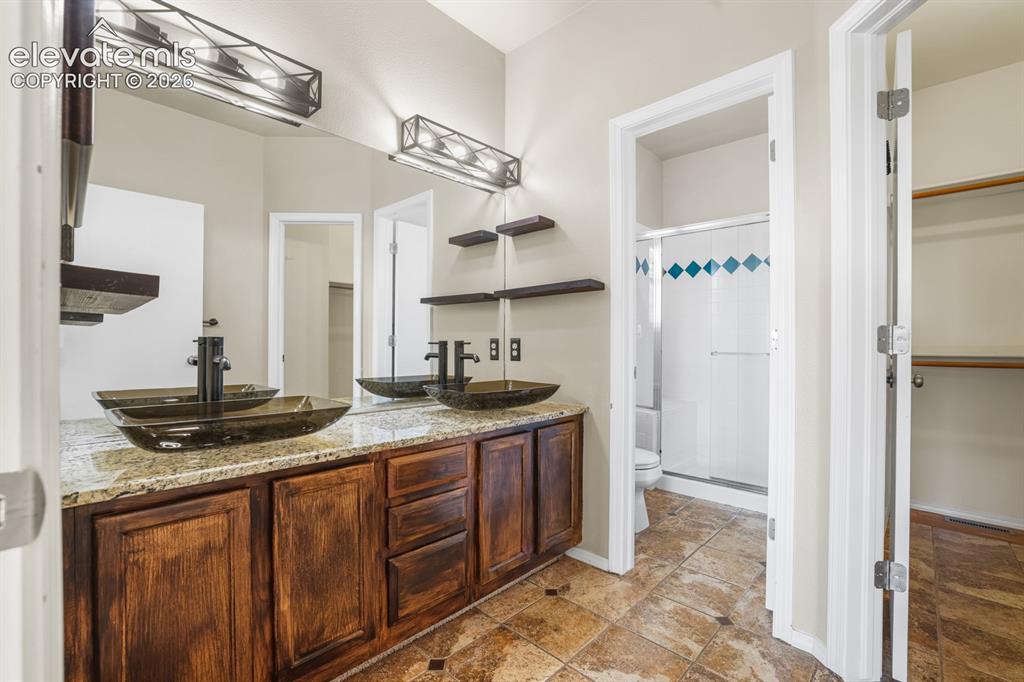 Image 13 of 37: Dual vessel sinks with wall-mounted faucets and a granite-look countertop