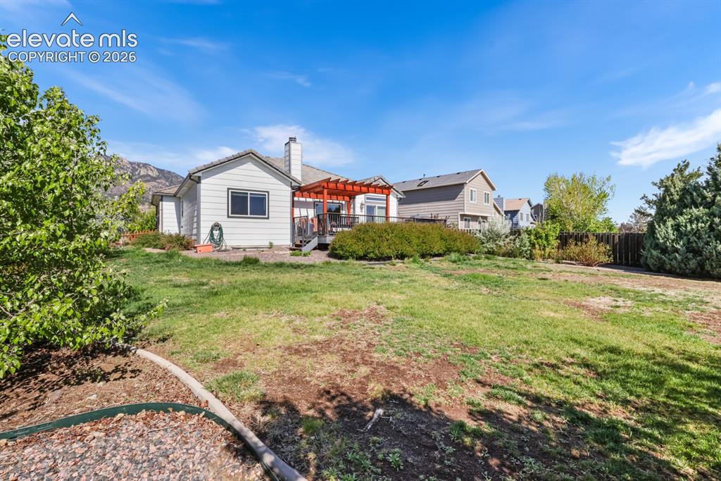 Image 33 of 37: Expansive backyard featuring a green lawn, mature landscaping, and a wood d