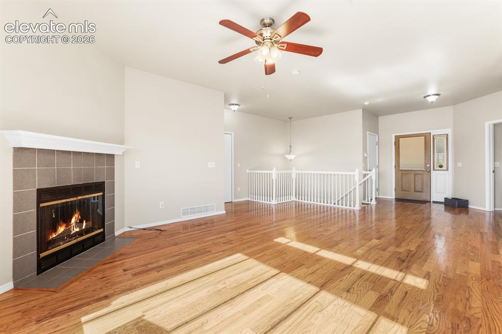 Image 5 of 37: Spacious living area featuring warm wood-finish flooring and a tiled firepl