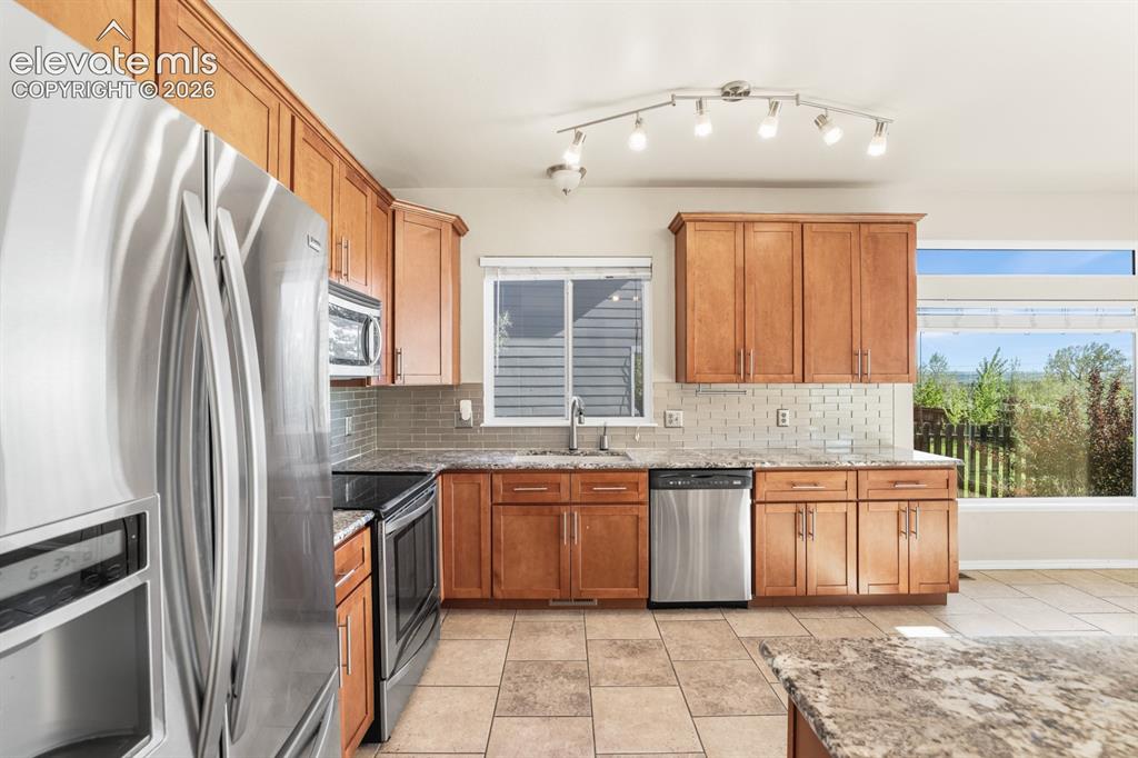 Image 7 of 37: Kitchen featuring stainless steel appliances, wood cabinetry, stone counter