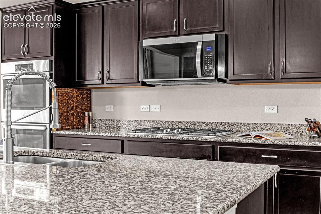 Image 12 of 49: Kitchen featuring dark wood cabinetry, speckled countertops, stainless stee