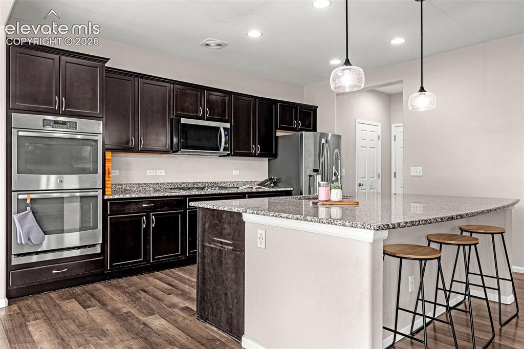 Image 13 of 49: Modern kitchen featuring dark wood cabinetry, stainless steel double wall o