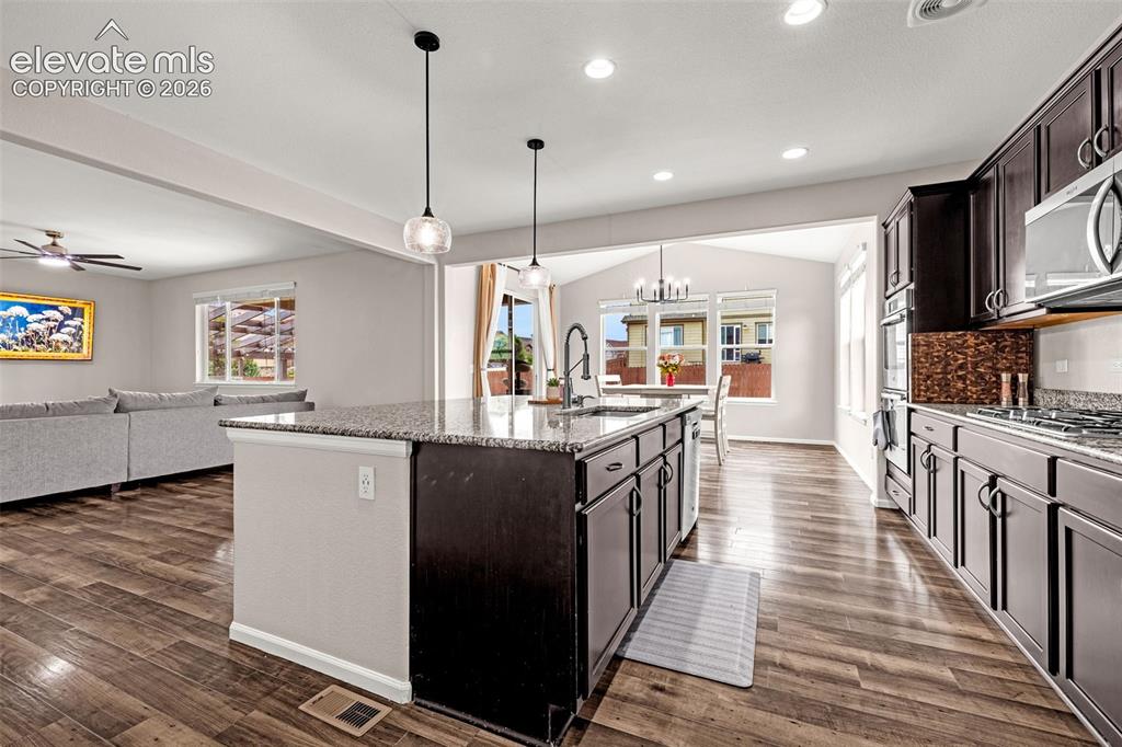 Image 14 of 49: Open-concept kitchen featuring an island with a built-in sink and pendant l