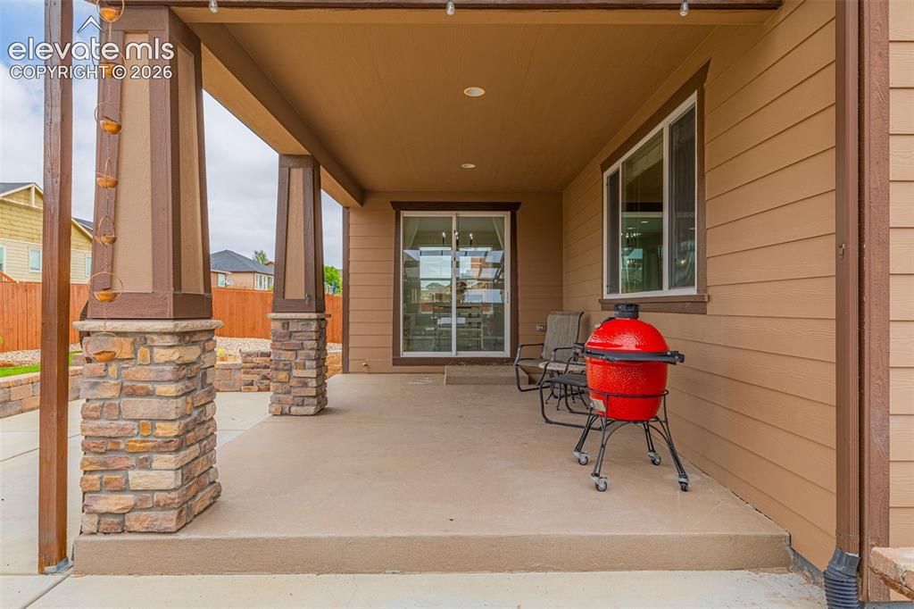 Image 36 of 49: Covered patio featuring stone-clad pillars, a concrete slab, and a sliding